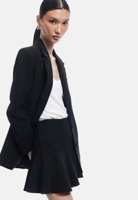 Sort skræddersyet blazer, hvid top og sort trekantet nederdel. Glat stof med struktureret design. Minimalistisk stil og moderne silhuet.