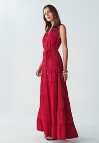 Červené, tiered maxi šaty bez rukávov s button-up predným zapínaním a viazaním v páse. Vyrobené z texturovanej látky s mriežkovým vzorom.