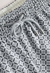 Close-up of gray and white patterned shorts with a tied drawstring threaded through metal eyelets on an elastic waistband.