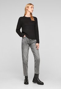 Pull en maille noir avec col rond, associé à un jean droit gris clair et des bottines noires à semelle épaisse.