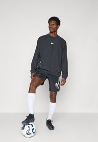 Nike sportsklærsett i svart med hvite detaljer, bestående av en langermet topp og shorts, kombinert med svarte fotballsko og hvite sokker.