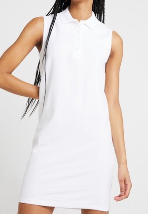 Witte mouwloze polojurk met kraag en drie knopen aan de voorkant. Gemaakt van gladde stof, met een minimalistisch ontwerp en een slanke pasvorm.