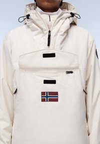 Witte waterproof capuchonjack met een voorzak, voorzien van een blauw en rood Noors vlaggenpatch en zwarte rits en klittenbandaccenten.