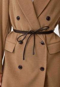 Dubbelzijdige, camelkleurige jas met een ceintuur in de taille, voorzien van donkere knopen, zijzakken en een zachte, wollen uitstraling.