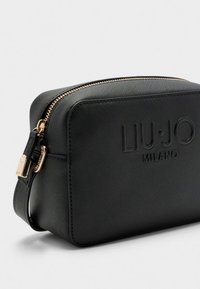 Geantă din material sintetic negru cu accesorii aurii, închidere cu fermoar și logo „LIU·JO MILANO” embossat pe față. Formă compactă, dreptunghiulară.