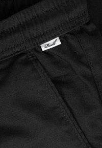 Tela de mezclilla negra con costuras detalladas y una pequeña etiqueta blanca de ropa que dice "Reell" cerca de una costura.