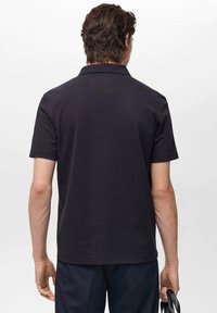 Svart kortärmad polo skjorta med krage, slät textur och bakvy. Tyget verkar lätt och lämpligt för avslappnad klädsel.