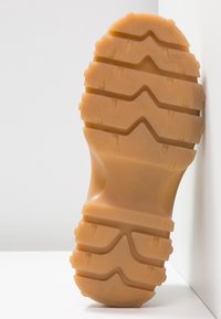 Gummisohle in hellem Braun mit multidirektionalen Profilmustern, Rillen und strukturierten Oberflächen für besseren Halt und Langlebigkeit.