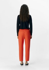 Un haut noir à manches longues et un pantalon rouge à taille élastique, avec des poches latérales et une coupe droite. Des sandales à talons noires complètent l'ensemble.