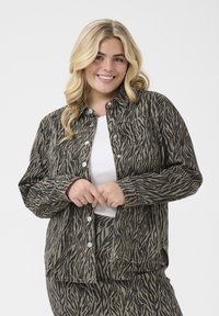 Button-up shirt in a black and beige zebra stripe pattern; features long sleeves, a relaxed fit, and metal snap buttons.