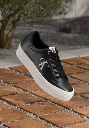 Svart lädersneaker med vit gummisula, som har runda skosnören och logodetalj på sidan och på tungan. Texturerat mönster på ytan.