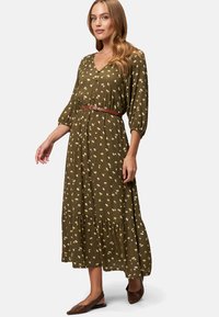 Olivengrünes Blumen-Kleid mit V-Ausschnitt, drei Viertel-Ärmeln, gestuften Saum und einem braunen Gürtel. Es hat ein Muster aus weißen und gelben Blumen.