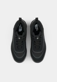 Des baskets noires avec une tige en maille texturée, un col rembourré et une semelle en caoutchouc avec des accents réfléchissants subtils, conçues pour le confort et le soutien.