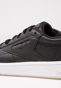 Baskets noires Reebok avec lacets noirs et semelle blanche texturée, affichant le logo Reebok cousu et l'Union Jack sur le panneau latéral.