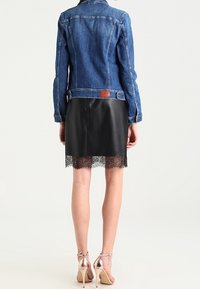 Džínová bunda s těsným střihem, doplněná černou koženou sukní s krajkovým lemem. Světle hnědá kovová spojovací součásti a lesklé metalické podpatky.