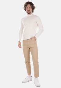 Maglione crema, pantaloni beige aderenti e sneakers bianche. Tessuto morbido, vestibilità slim, design minimalista con scollatura a costine e cuciture sottili.