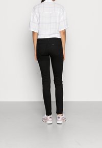 Jeans ajustados negros combinados con una camisa blanca de cuadros. El conjunto se completa con unas zapatillas blancas y rosas. Costuras visibles y un diseño ceñido.