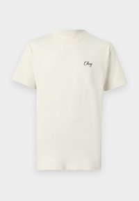 Εκρού κοντομάνικο T-shirt με στρογγυλή λαιμόκοψη και μικρό μαύρο κείμενο "Obey" στο αριστερό στήθος.