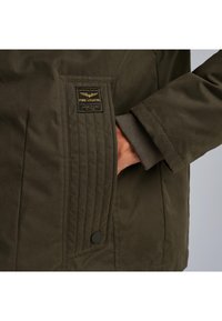 Maslinasto zelena jakna s teksturiranom tkaninom, opremljena preklopom džepa s kviltom, logotipom i detaljem s dugmetom.