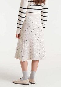 Falda beige hasta la rodilla con lunares negros, hecha de una tela suave. Combinada con calcetines grises y mocasines de color claro.