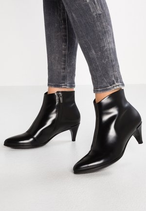 Bottines en cuir noir avec fermetures éclair latérales et talons bas portées avec un jean skinny noir délavé.
