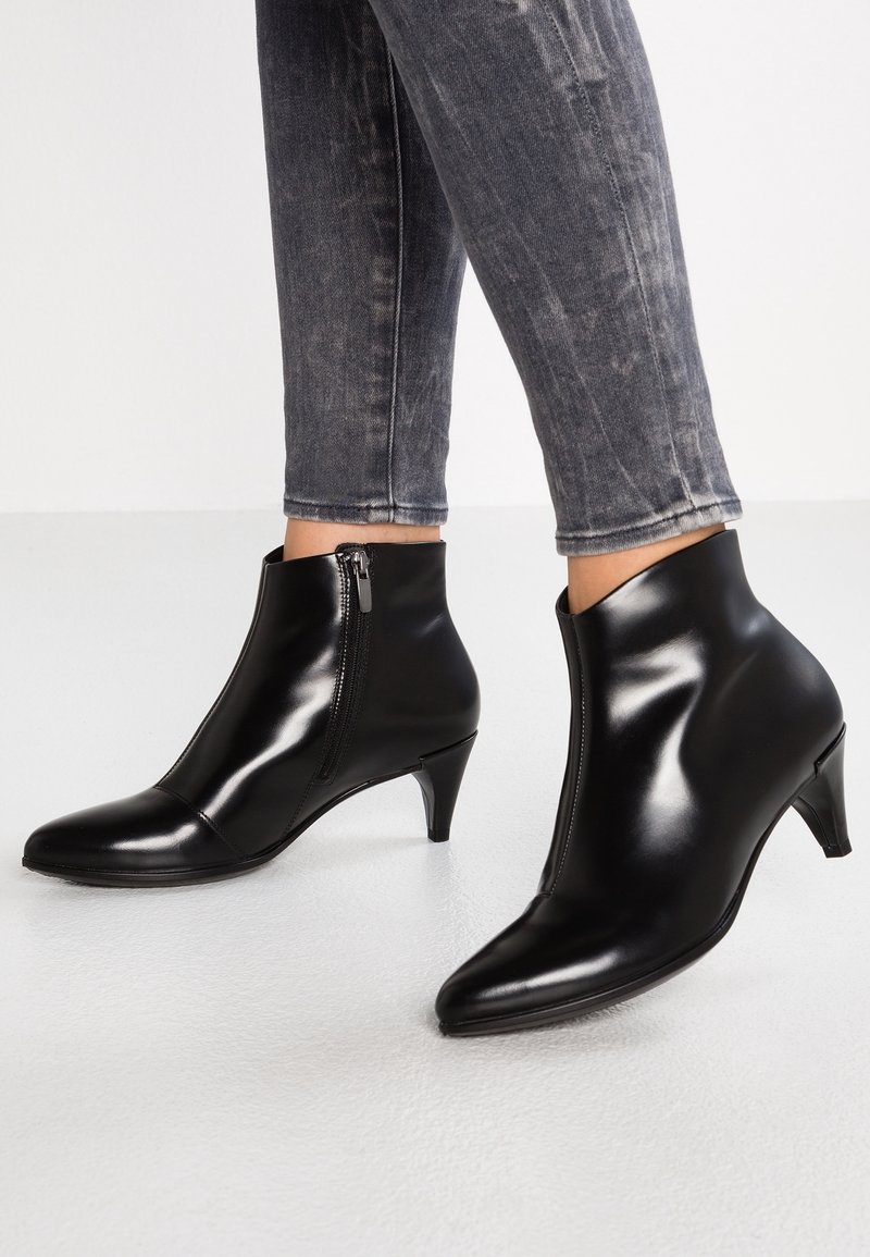 Bottines en cuir noir avec fermetures éclair latérales et talons bas portées avec un jean skinny noir délavé.