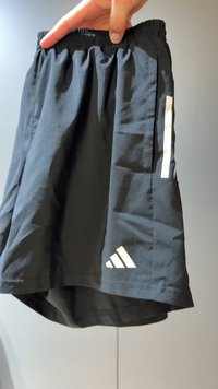 Zwarte sportkorte broek gemaakt van lichtgewicht stof, met een elastische tailleband, zijzakken en drie witte strepen aan de zijkant.