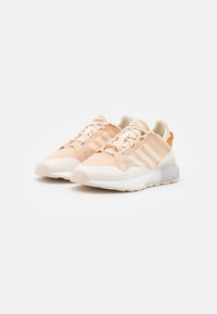 Light peach sneakers with textured mesh upper, cream accents, white sole, and three horizontal stripes on the sides.