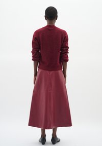 Ribaga burgundivärvi kampsun koos pikka, siledast burgundivärvi nahkse seelikuga. Mudel kannab musti loafer'eid. Lihtne, minimalistlik disain.