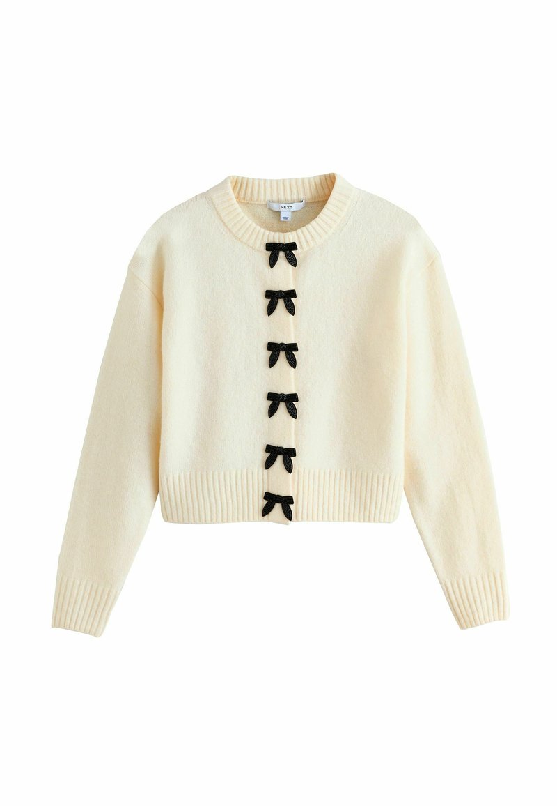 Cream-colored cropped sweater with ribbed hem and cuffs, featuring six black bow accents along the button closure. Soft texture.