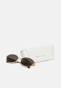 Ochelari Michael Kors cu lentile ovale negre și ramă din metal auriu, însoțiți de un capac protecție alb care prezintă numele mărcii.