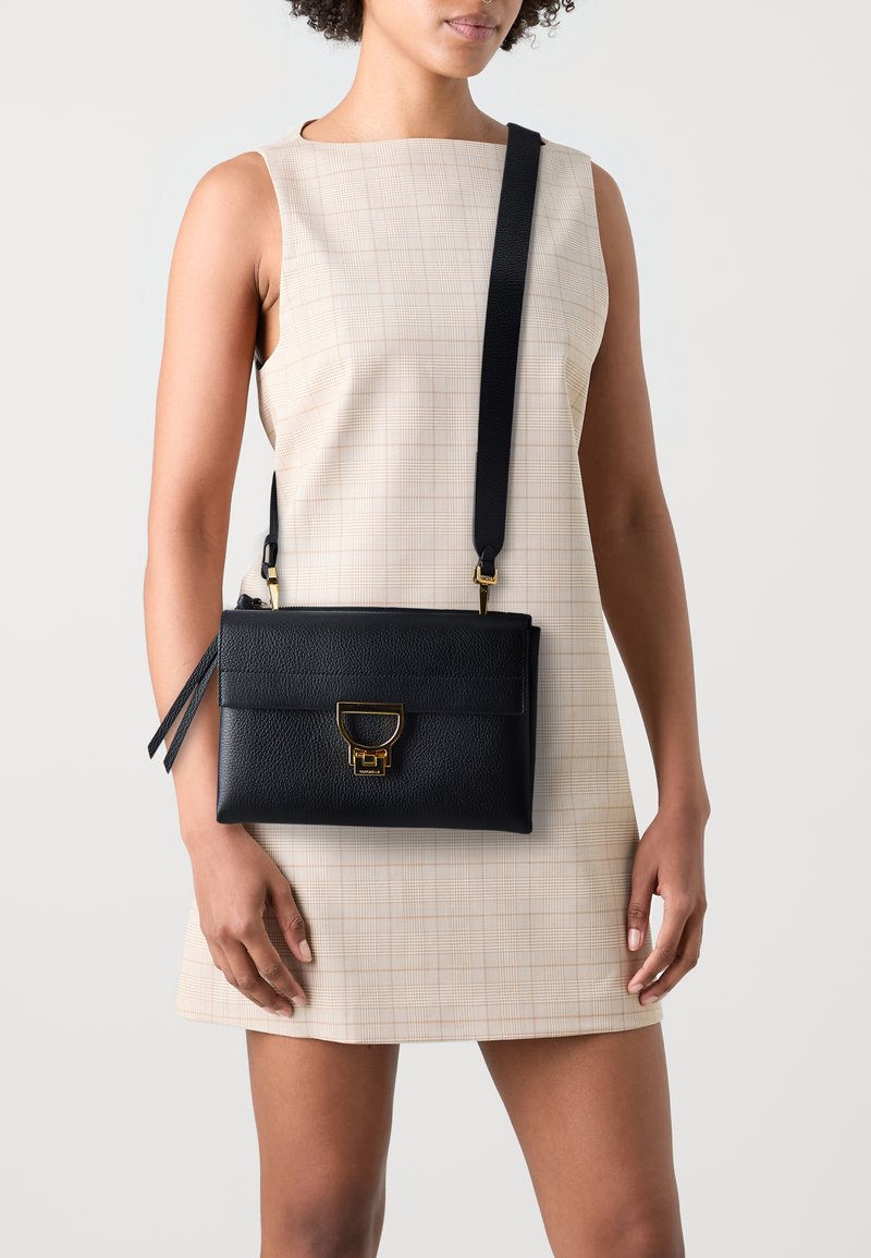 Sort lædercrossbody taske med en struktureret form, guldhardware og lukning med frontlås. Tekstureret overflade og aftagelig rem.