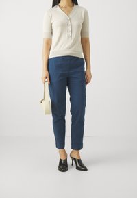 Beżowy kardigan z krótkim rękawem, z dekoltem w kształcie litery V i detalami w postaci guzików, zestawiony z granatowymi spodniami i czarnymi klapkami na obcasie; minimalistyczny design.