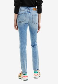 Ljusblå denimjeans, slim fit, medelhög midja, bakfickor och en brun logotyp-lapp vid midjan. Matchas med flerfärgade sneakers.