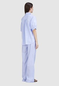 Hellblau gestreiftes Hemd mit kurzen, puffartigen Ärmeln und Rückenschlitz, kombiniert mit passenden, weit geschnittenen Hosen aus weichem Stoff.