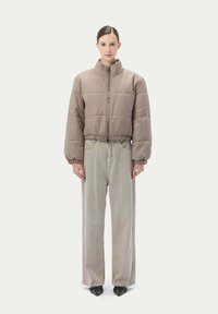 Puffjacka i ljusbrunt tyg med hög krage, elastisk nederkant och ribbade manschetter, tillsammans med vida beige byxor och svarta skor.