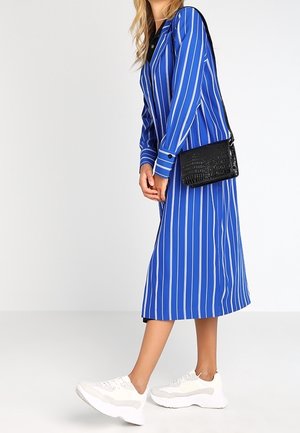 Blau-weißer gestreifter langer Dress mit Kragen, kombiniert mit einer schwarzen strukturierten Umhängetasche und weißen Sneakers.