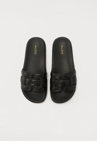 Sandales slides noires à semelle plate, en cuir lisse, avec une large bride ornée d'une boucle géométrique et d'un logo doré.