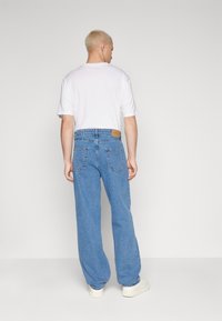 Light blue denim jeans with a relaxed fit, featuring two back pockets, a leather patch at the waistband, and ample length for a loose appearance.