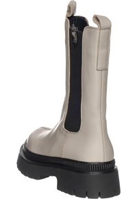 Botín beige de cuero con panel lateral elástico negro y suela de goma negra texturizada. Cuenta con una lengüeta en el talón para facilitar su uso.