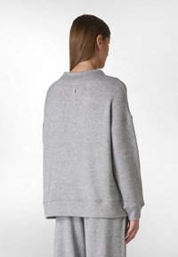 Sudadera gris de corte holgado, con tejido texturizado, puños acanalados y una pequeña etiqueta en la parte posterior, complementada con pantalones grises a juego.
