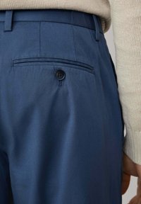 Pantalones azul marino con una textura suave, que cuentan con un bolsillo trasero con un único botón negro y detalles de costura a medida.