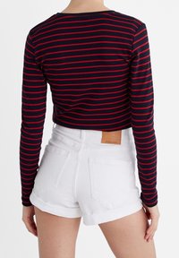 Musta ja punaisilla raidoilla varustettu pitkähihaine paita, jossa on pyöreä kaula-aukko, yhdistetty valkoisiin denimpö shortsit, joissa on käänteet ja takataskut.