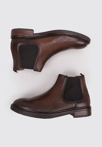 Bottines Chelsea en cuir marron avec des panneaux élastiques sur les côtés, un bout arrondi et un talon empilé avec une texture lisse.