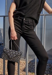 Black knitted top paired with black fitted jeans. A beaded black and white hexagon-patterned clutch bag is held in the hand.