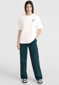 Witte katoenen T-shirt met korte mouwen en een grafische print, gecombineerd met teal corduroy cargobroek met zijzakken en een relaxte pasvorm.
