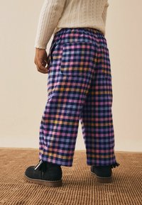 Lilla, pink og sorte ternede bukser lavet af blødt stof med elastik i livet og to baglommer, parret med sorte ankelstøvler.