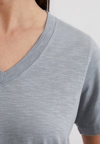 Grijze V-hals t-shirt met korte mouwen, gemaakt van een zachte, gestructureerde stof met een subtiel heatherpatroon. Close-up van de halslijn.