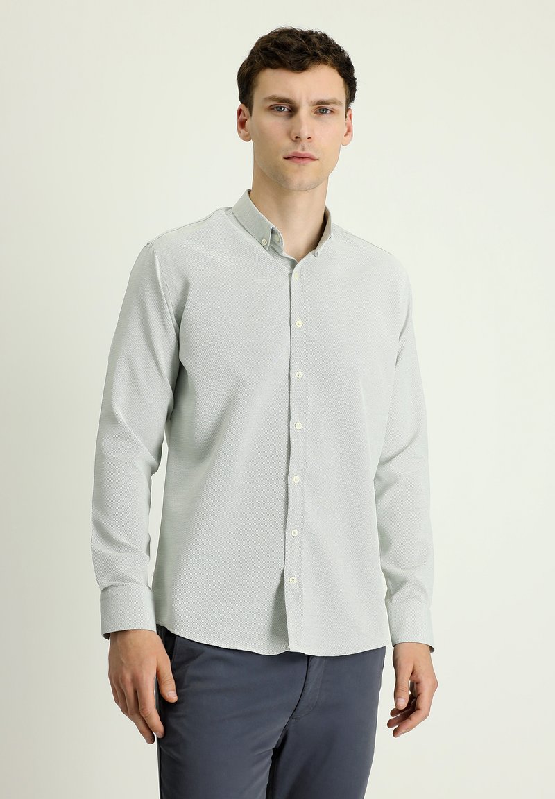 Camicetta gris chiaro con bottoni, un motivo testurizzato, maniche lunghe e colletto classico, abbinata a pantaloni blu scuro.