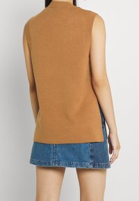 Brązowy dzianinowy top bez rękawów z wysokim kołnierzem i prążkowanymi krawędziami, zestawiony z dżinsową mini spódniczką, prezentujący luźny krój.